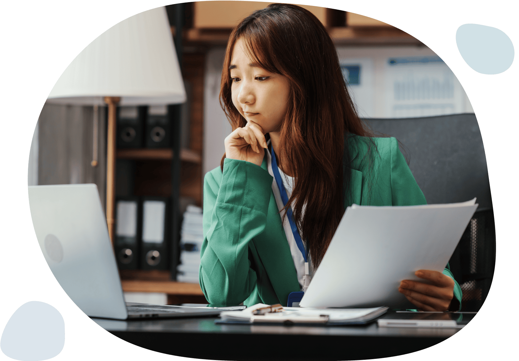 A woman in a green jacket sits at a desk, focused on her laptop, engrossed in her work.